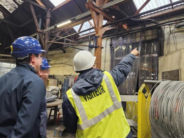 Des personnes de dos dans un atelier de métallurgie, une porte un gilet visiteur